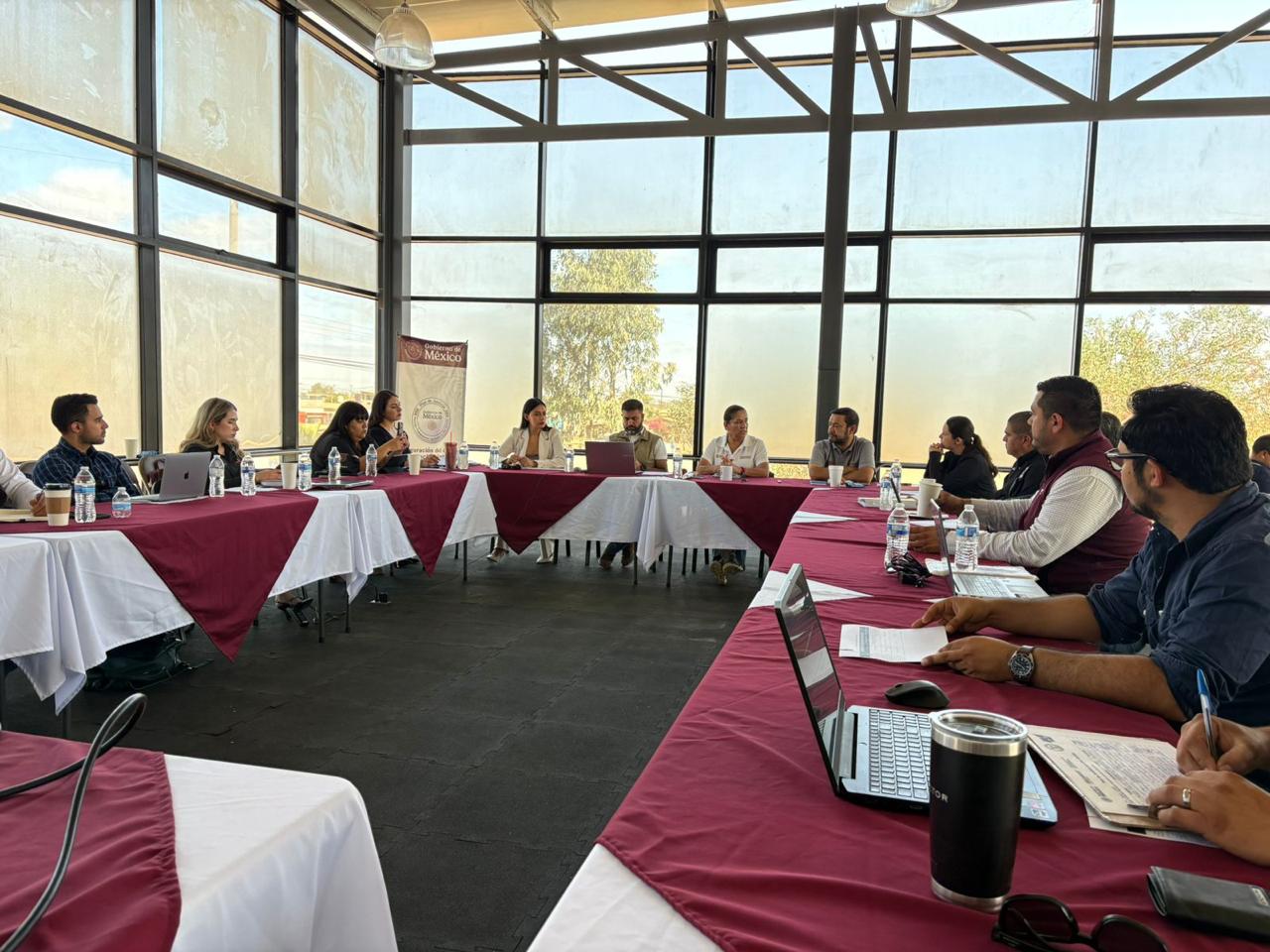 Mesa de coordinación institucional en San Quintín, con manteles guinda y equipos de trabajo alrededor.