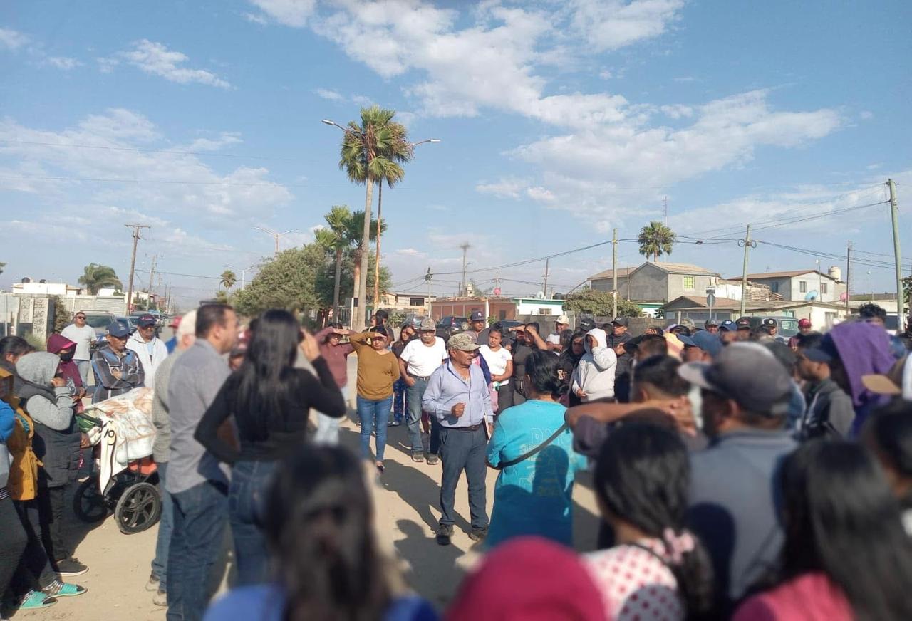 Asamblea vecinal a media calle con palmeras al fondo.