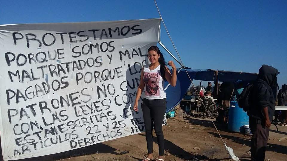Mujer joven frente a una manta con demandas de jornaleros del Valle.