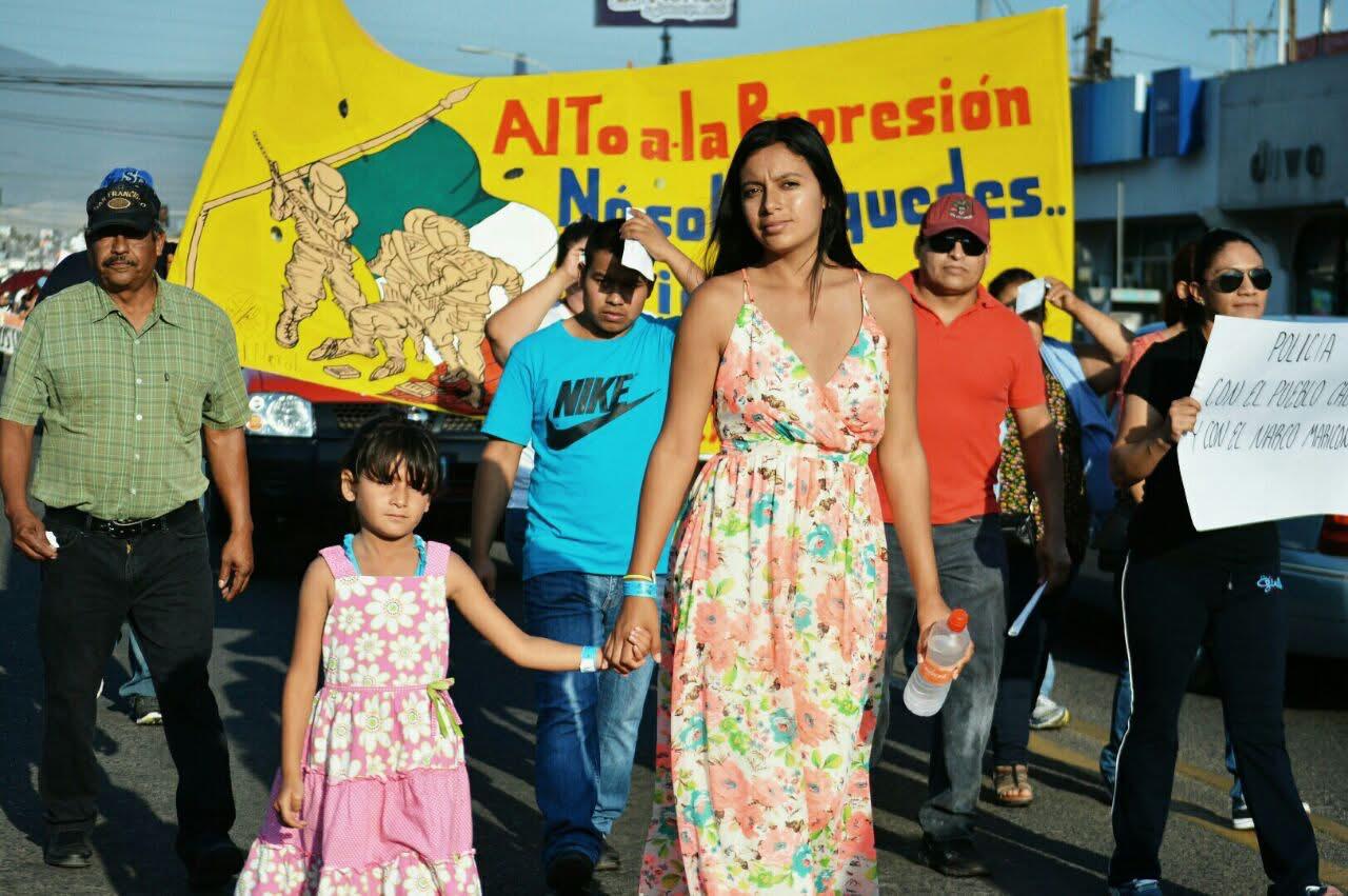 Contingente en una marcha contra la represión, con manta amarilla y familias caminando.